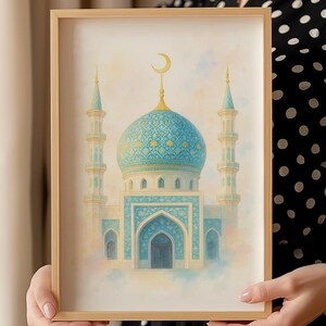 Puede incluir: Una impresión en acuarela enmarcada de una mezquita con una cúpula azul y minaretes. La obra de arte presenta una luna creciente y detalles arquitectónicos intrincados. El marco es de madera clara, y el estilo general es suave y artístico.