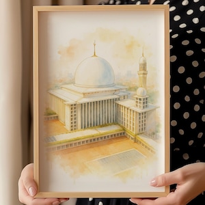 May include: Watercolor print of a mosque in a light wooden frame. The artwork depicts a white-domed building with a minaret, set against a soft, yellow and orange sky. The architectural details are rendered in a delicate, artistic style.
