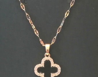 May include: Gold-toned necklace with a clover pendant. The pendant is encrusted with small, clear gemstones, and the chain has a delicate, linked design. The necklace is displayed against a dark background.