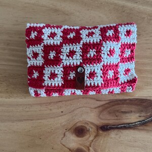 May include: A small red and white crocheted pouch with a brown leather closure. The pouch has a geometric pattern.