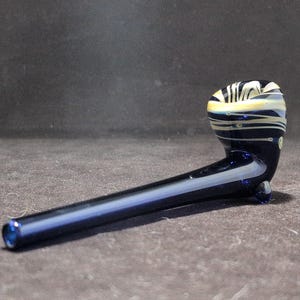 Peut inclure: Une pipe en verre bleu avec des motifs en spirale blancs et noirs. La pipe a un long manche incurvé et un bol en haut.