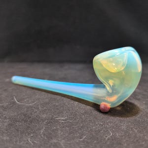 Op de afbeelding: Een lichtblauwe glazen pijp met een ronde kom en een lange, dunne steel. De pijp heeft een lichtblauw en wit swirl-patroon.