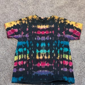 May include: A black t-shirt with a vibrant tie-dye pattern. The design features horizontal bands of yellow, pink, blue, and purple, creating a colorful and eye-catching effect. The shirt is made of a soft material.