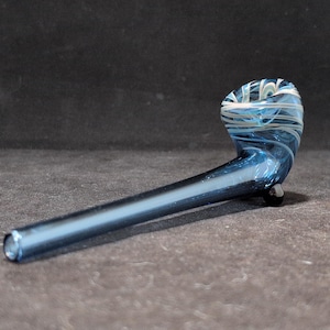 Peut inclure: Une pipe en verre bleu avec des motifs en spirale blancs. La pipe a une tige longue et fine et un bol en forme de petite tasse.