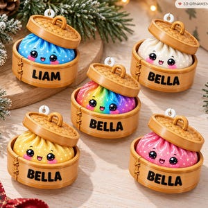 May include: Five 3D ornaments shaped like dumplings in bamboo steamers. One blue dumpling labeled LIAM, and four dumplings labeled BELLA in white, rainbow, yellow, and pink. Each has a smiling face with large black eyes and pink cheeks.