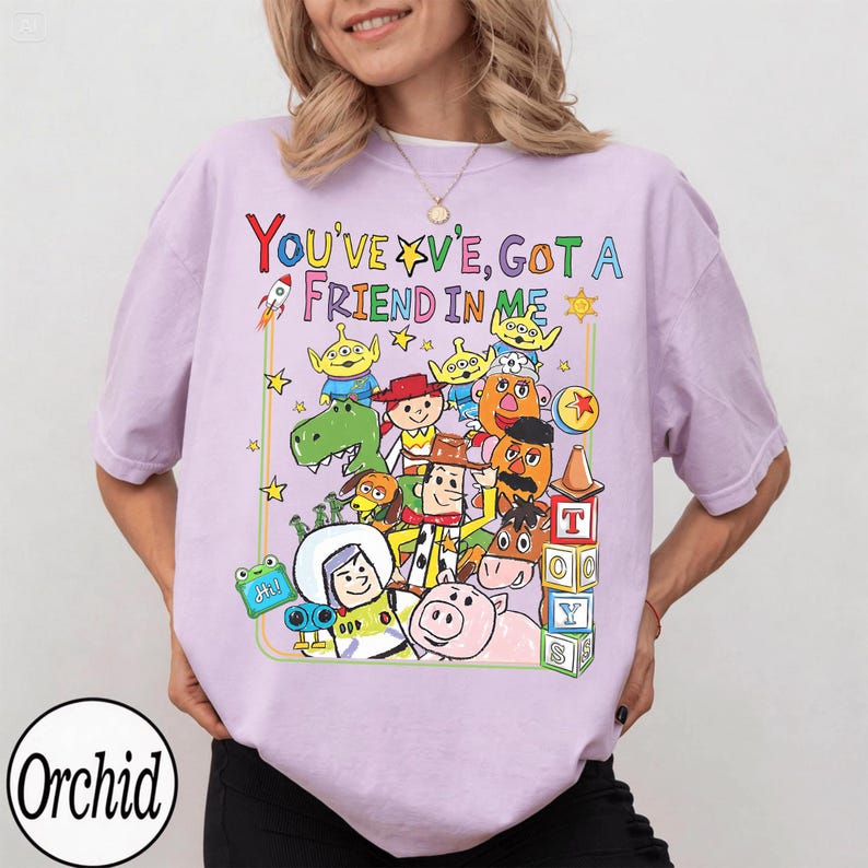May include: A lilac t-shirt with a vibrant graphic of animated characters and the text "YOU'VE GOT A FRIEND IN ME". The design includes a rocket, stars, and a sun. The shirt has a round neck and short sleeves.
