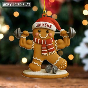 May include: A gingerbread man Christmas ornament with a Santa hat and a red and white scarf. The gingerbread man is lifting weights and has the name "JACKSON" on his hat. The ornament is a 2D flat design.
