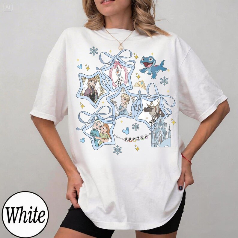 Może przedstawiać: Biała koszulka z grafiką przedstawiającą postacie z filmu "Kraina Lodu". Projekt zawiera obrazy Elsy, Anny, Olafa, Kristoffa i Svena, obramowane niebieskimi wstążkami i płatkami śniegu. Wyświetlane jest r&oacute;wnież słowo "FROZEN".