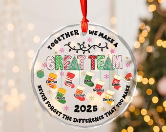 May include: A clear, round Christmas ornament with a red ribbon. The ornament has the text "TOGETHER WE MAKE A GREAT TEAM" and "NEVER FORGET THE DIFFERENCE THAT YOU MAKE" with names and the year 2025.