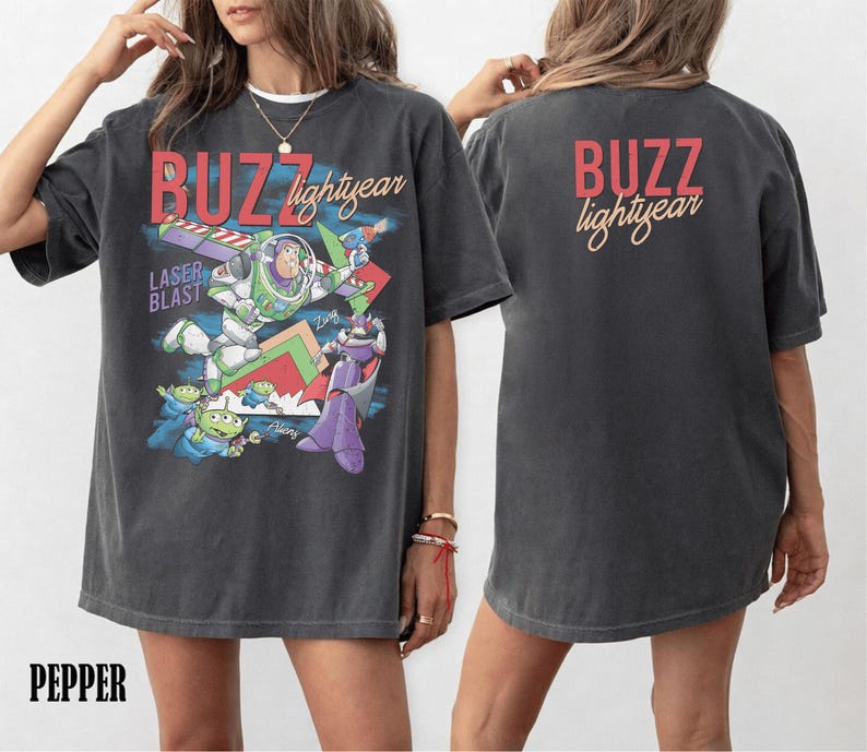 May include: Dark gray t-shirt featuring a graphic of Buzz Lightyear with the text "BUZZ lightyear" in red and yellow. The front of the shirt has a colorful design with the words "LASER BLAST". The back of the shirt also has the text "BUZZ lightyear".