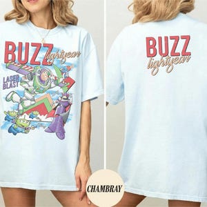 May include: Light blue t-shirt featuring a graphic of Buzz Lightyear with the text "BUZZ lightyear" in red and yellow. The front of the shirt shows Buzz in action with the words "LASER BLAST". The back of the shirt has the text "BUZZ lightyear".
