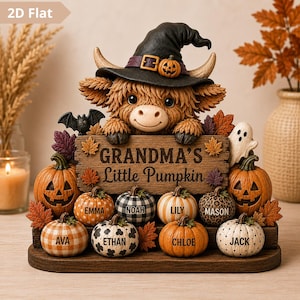 May include: A decorative tabletop display featuring a brown Highland cow wearing a black witch hat with a small pumpkin accent. The cow holds a wooden sign reading "GRANDMA'S Little Pumpkin" surrounded by several small pumpkins labelled with names.