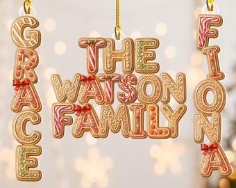 May include: Gingerbread-style Christmas ornaments spelling out "GRACE", "THE WATSON FAMILY", and "FIONA". Each letter is decorated with icing, candy, and red bows, hanging from gold cords against a blurred background of lights.