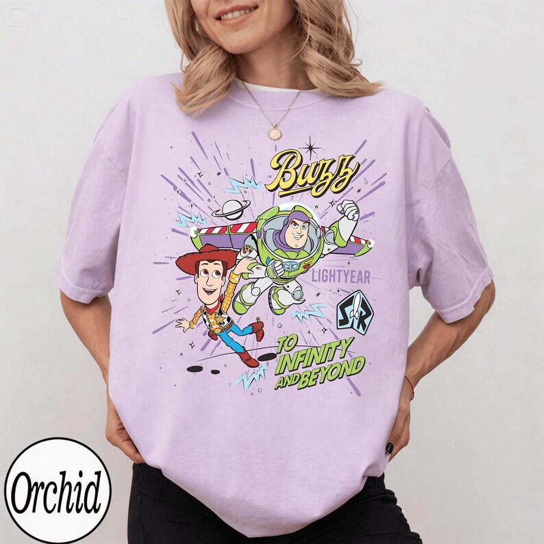 May include: A light purple t-shirt featuring a graphic of Buzz Lightyear and Woody from Toy Story. The design includes the words "Buzz Lightyear" and "To Infinity and Beyond" in a playful font. The shirt has short sleeves.