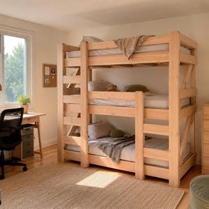 May include: A triple-stacked bunk bed frame constructed from light-colored natural wood, featuring three levels of sleeping platforms with integrated side ladders and safety rails, positioned in a room with a desk and a wooden dresser.
