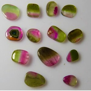 May include: A collection of 12 green, pink, and black tourmaline gemstones. The gemstones are various shapes and sizes, and some have a unique, iridescent sheen.