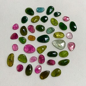 May include: Assortment of green, blue, pink, and yellow gemstones. The gemstones are faceted and have a variety of shapes and sizes.