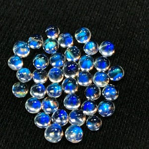 Op de afbeelding: Een verzameling van iriserende blauwe maansteen cabochons, elk met een uniek patroon van blauw en wit.