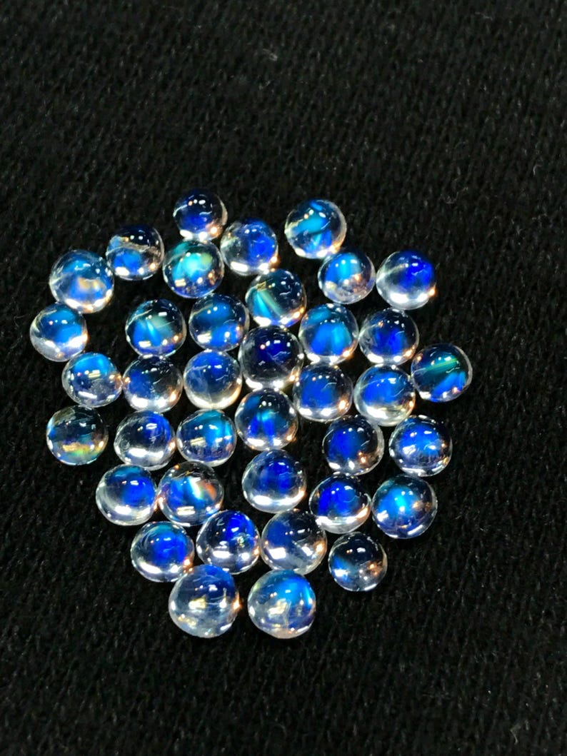 Op de afbeelding: Een verzameling van iriserende blauwe maansteen cabochons, elk met een uniek patroon van blauw en wit.