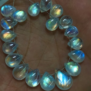 May include: A string of iridescent, teardrop-shaped moonstone beads. The beads are strung on a thin, silver wire. Each bead displays a play of colour, with flashes of blue, yellow, and orange. The beads are translucent and have a smooth, polished surface.