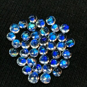Op de afbeelding: Een verzameling van iriserende blauwe en witte edelsteen cabochons. De cabochons zijn rond en hebben een glad, gepolijst oppervlak.