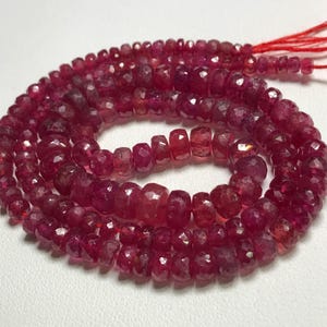May include: A strand of ruby red gemstone beads. The beads are faceted and have a slightly irregular shape. The beads are strung on a red thread.