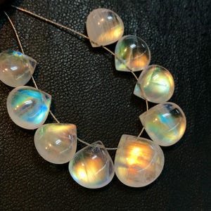 May include: A strand of iridescent rainbow moonstone teardrop beads. The beads are strung on a thin wire and are arranged in a semi-circle.