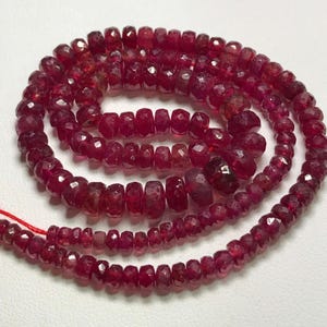 May include: A strand of deep red ruby beads, faceted and polished, with a slightly irregular shape. The beads are strung on a thin red thread.