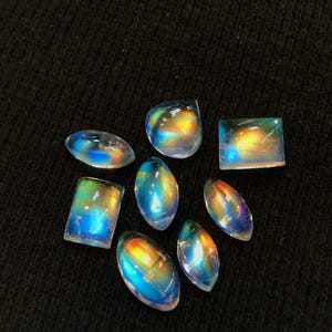 Puede incluir: Una colecci&oacute;n de siete cabujones de piedras preciosas iridiscentes en varias formas y tama&ntilde;os. Las piedras son una mezcla de formas ovaladas, rectangulares y cuadradas. Las piedras son de color azul claro con un brillo arco&iacute;ris.