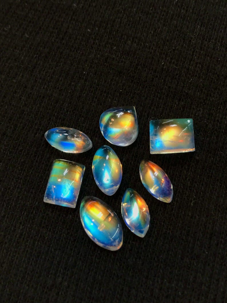 Puede incluir: Una colecci&oacute;n de siete cabujones de piedras preciosas iridiscentes en varias formas y tama&ntilde;os. Las piedras son una mezcla de formas ovaladas, rectangulares y cuadradas. Las piedras son de color azul claro con un brillo arco&iacute;ris.