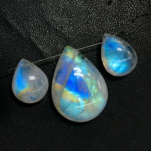 May include: Three teardrop-shaped moonstone pendants with iridescent blue and white colours. The pendants are strung on a silver wire.