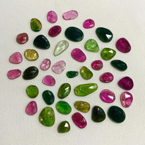 May include: A collection of 30 loose gemstones in various shades of green, pink, and yellow. The gemstones are cut in a variety of shapes, including oval, round, and pear.
