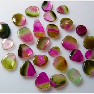 May include: A collection of 25 colorful, smooth, and polished gemstones. The stones are various shades of green, pink, and brown. They are all roughly oval shaped and have a natural, unpolished look.