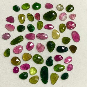 May include: A collection of green, pink, and yellow gemstones. The gemstones are various shapes and sizes and have a smooth, polished finish.