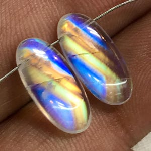 May include: Two oval-shaped iridescent clear quartz beads with blue, green, and yellow colours.