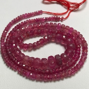 May include: A strand of pink ruby beads, faceted and polished, strung on a red thread. The beads are of varying sizes and shapes, creating a textured and elegant look.