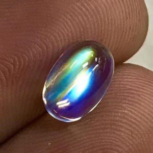 May include: An oval-shaped gemstone with a mesmerizing play of color. The stone transitions from blue to green and yellow, creating a rainbow effect. The polished surface reflects light, showcasing its internal brilliance.