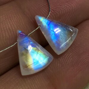 May include: Two iridescent moonstone triangle beads. The stones show a play of colour with hues of blue, yellow, and purple. Each bead is strung on a thin silver wire, ready for jewellery making. The stones are translucent.