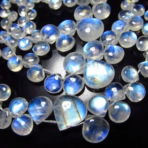 May include: A strand of iridescent moonstone beads in a teardrop shape. The beads are strung on a white thread and have a blue and white iridescent sheen.
