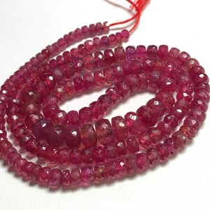 May include: A strand of ruby red gemstone beads. The beads are faceted and have a slightly irregular shape. The beads are strung on a red thread.