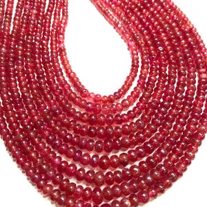 May include: A strand of red ruby beads, with a smooth, round shape. The beads are strung together on a clear thread, and the strand is laid out in a fan shape.