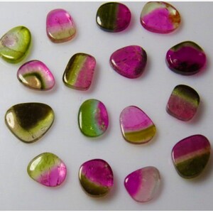 May include: Assortment of 15 green, pink, and black gemstone cabochons. The cabochons are all different shapes and sizes, but they are all smooth and polished.