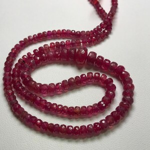May include: A strand of ruby red gemstone beads, strung on a thread, forming a necklace. The beads are faceted and have a slightly irregular shape.