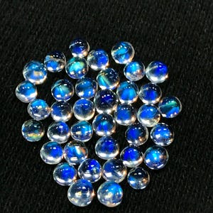 Op de afbeelding: Een verzameling van iriserende blauwe en witte edelsteen cabochons. De cabochons zijn rond en hebben een glad, gepolijst oppervlak.
