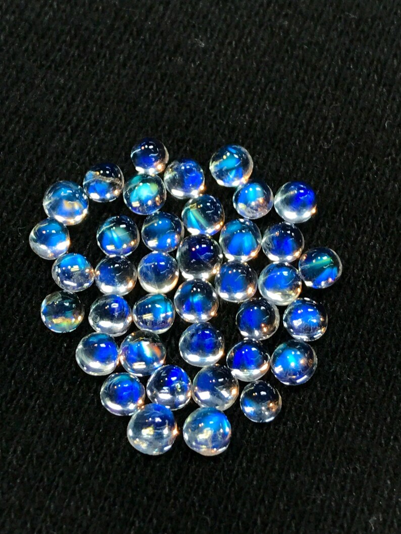 Op de afbeelding: Een verzameling van iriserende blauwe en witte edelsteen cabochons. De cabochons zijn rond en hebben een glad, gepolijst oppervlak.