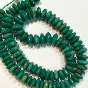 May include: A strand of green gemstone beads, each bead is faceted and has a slightly oval shape.