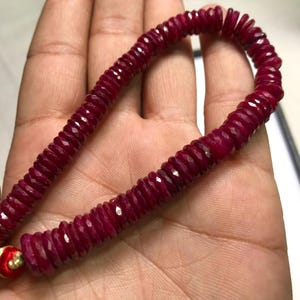 May include: A strand of deep red ruby beads, each bead is faceted and shaped like a small, flat disc. The beads are strung on a thin cord and are approximately 1/2 inch in diameter.