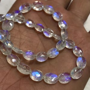 May include: A strand of iridescent white oval-shaped gemstone beads. The beads have a rainbow sheen.