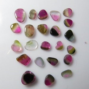 May include: Assortment of 25 loose, natural, multi-colored gemstones. The stones are various shades of pink, green, black, and clear. The stones are all different shapes and sizes.