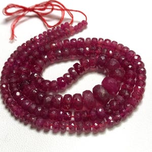 May include: A strand of deep red ruby beads, faceted and strung on a red thread. The beads are approximately 4mm in diameter and have a polished, faceted finish.